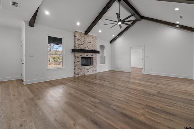 unfurnished living room featuring beam ceiling, ceiling fan, a fireplace, and light wood-type flooring