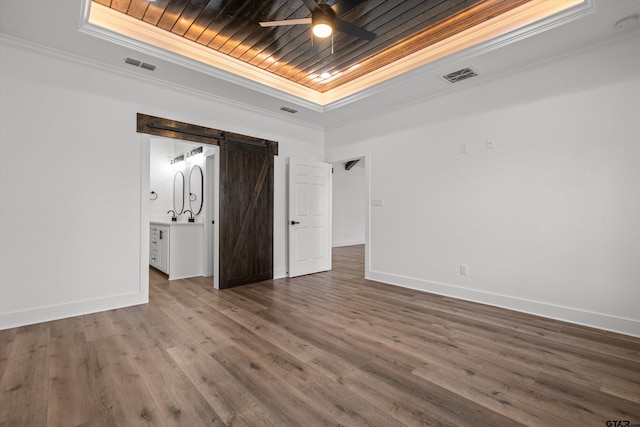 unfurnished bedroom featuring a tray ceiling, a barn door, hardwood / wood-style flooring, and ornamental molding