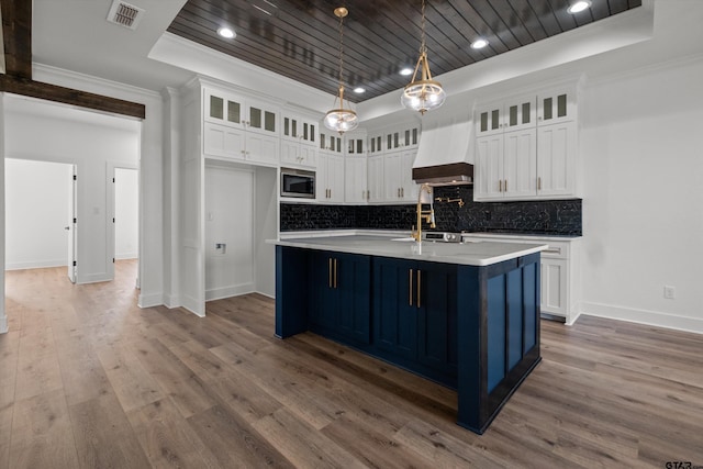 kitchen featuring premium range hood, a tray ceiling, pendant lighting, white cabinetry, and an island with sink