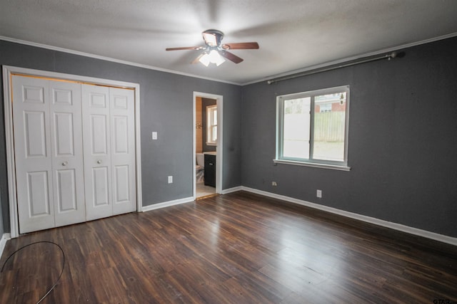 unfurnished bedroom featuring connected bathroom, dark hardwood / wood-style flooring, ceiling fan, crown molding, and a closet