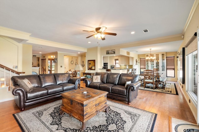 living room with crown molding, stairs, ceiling fan with notable chandelier, light wood-style floors, and visible vents