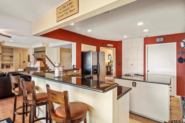 kitchen with dark countertops, a center island, a breakfast bar, stainless steel fridge, and recessed lighting