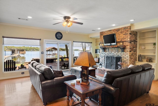 living area featuring crown molding, ceiling fan, light wood finished floors, a fireplace, and visible vents