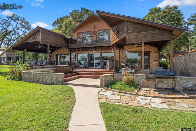 rear view of property with a balcony, a yard, a covered hot tub, ceiling fan, and a patio area