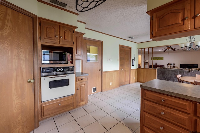 6001 Huntington Dr, Tyler, TX 75703 - kitchen featuring white oven, stainless steel microwave, a wainscoted wall, brown cabinets, and a textured ceiling