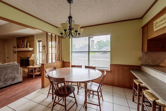 6001 Huntington Dr, Tyler, TX 75703 - dining space featuring a wainscoted wall, a brick fireplace, a textured ceiling, light tile patterned floors, and ornamental molding