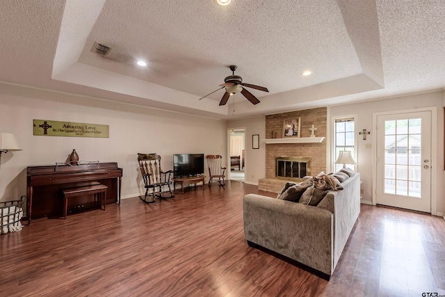 6001 Huntington Dr, Tyler, TX 75703 - living area featuring a raised ceiling, a textured ceiling, wood finished floors, a ceiling fan, and a fireplace