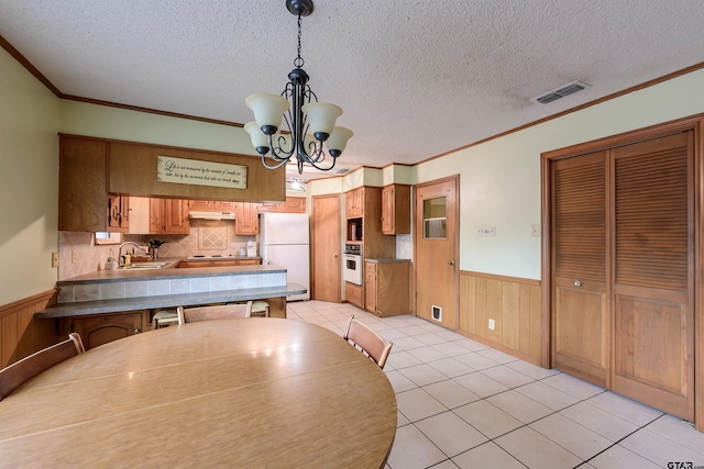 6001 Huntington Dr, Tyler, TX 75703 - dining area with a wainscoted wall, a chandelier, ornamental molding, a textured ceiling, and light tile patterned floors
