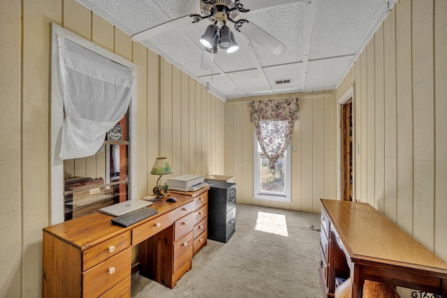 carpeted office space featuring ceiling fan and wood walls