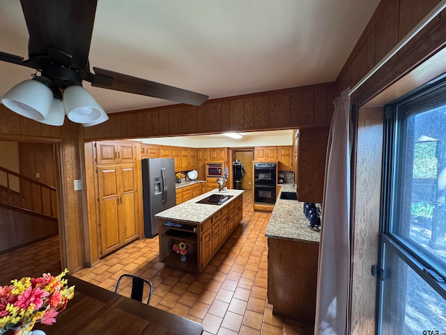 kitchen featuring black appliances, wooden walls, a kitchen island, and ceiling fan