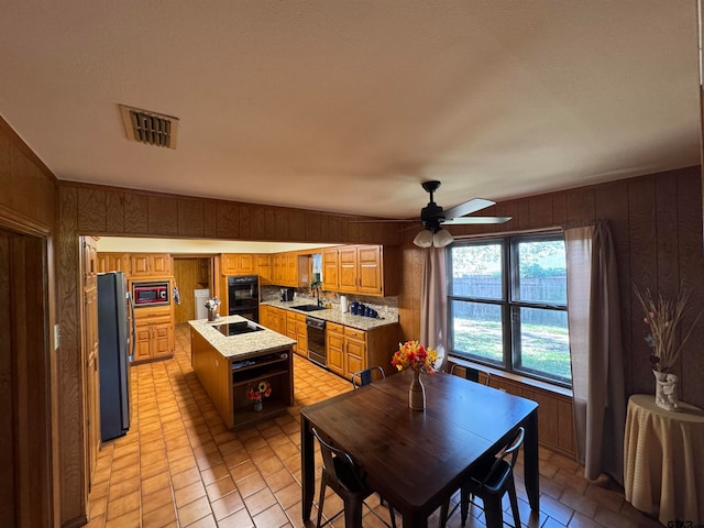 kitchen with wood walls, black appliances, sink, and a center island