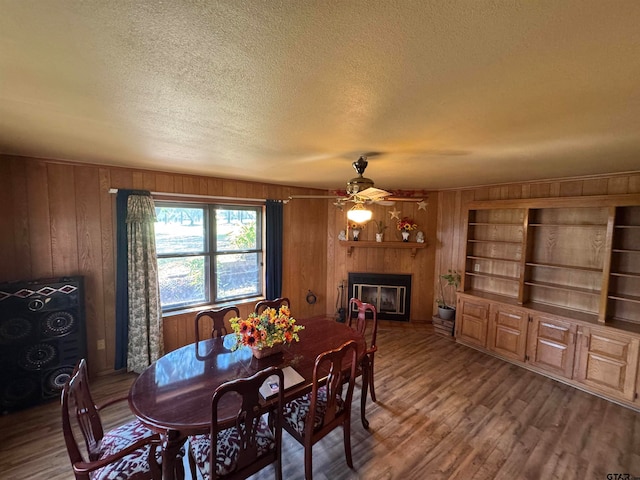 dining area featuring wood walls, hardwood / wood-style flooring, ceiling fan, and a textured ceiling