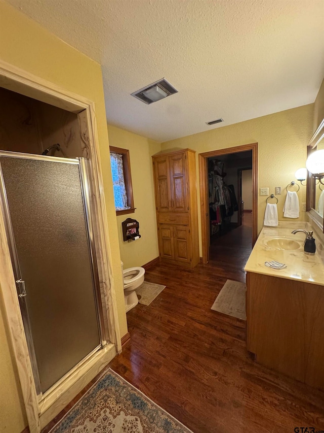 bathroom featuring walk in shower, a textured ceiling, hardwood / wood-style floors, vanity, and toilet