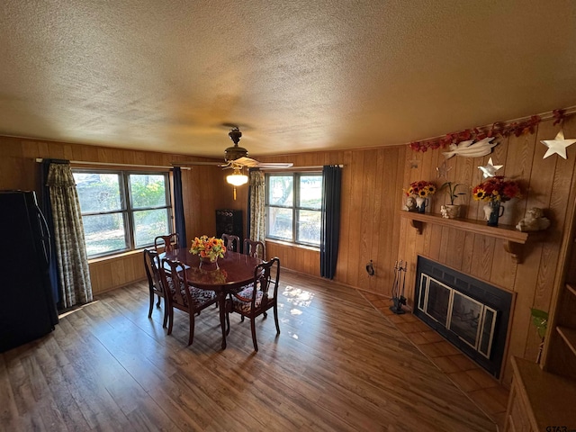 dining space with hardwood / wood-style floors, a tiled fireplace, a textured ceiling, and ceiling fan