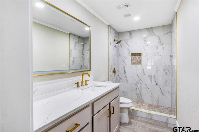 bathroom with hardwood / wood-style floors, vanity, toilet, ornamental molding, and tiled shower