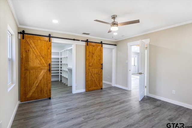 unfurnished bedroom with ceiling fan, a spacious closet, dark wood-type flooring, a barn door, and ornamental molding