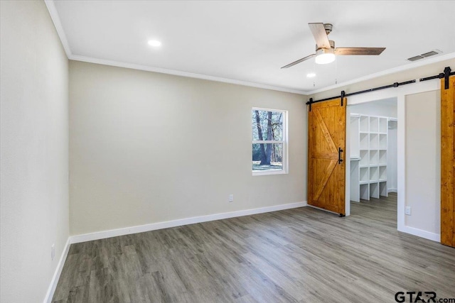 unfurnished bedroom with ceiling fan, a barn door, a spacious closet, and crown molding