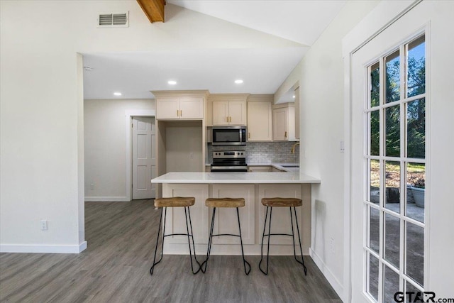 kitchen featuring lofted ceiling with beams, sink, appliances with stainless steel finishes, kitchen peninsula, and a breakfast bar area