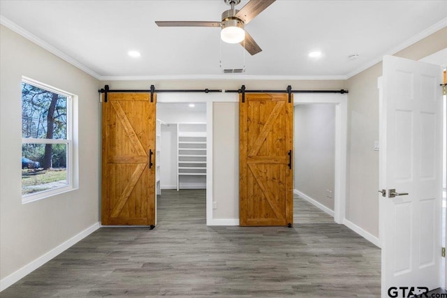 unfurnished bedroom with a walk in closet, ceiling fan, crown molding, a barn door, and a closet