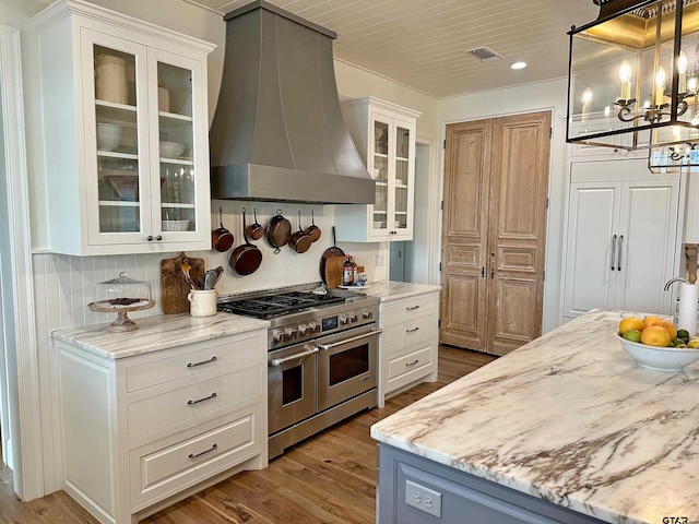 kitchen featuring visible vents, range with two ovens, wall chimney exhaust hood, wood finished floors, and white cabinetry