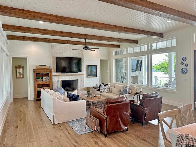 living area featuring beam ceiling, a brick fireplace, baseboards, and light wood finished floors