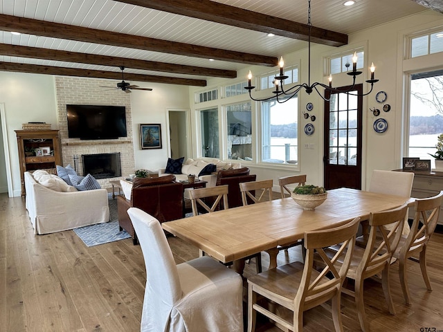 dining area featuring beam ceiling, a fireplace, light wood-style flooring, and a healthy amount of sunlight