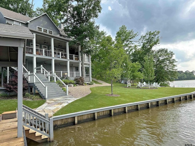 back of property with a water view, a lawn, stairway, ceiling fan, and a balcony