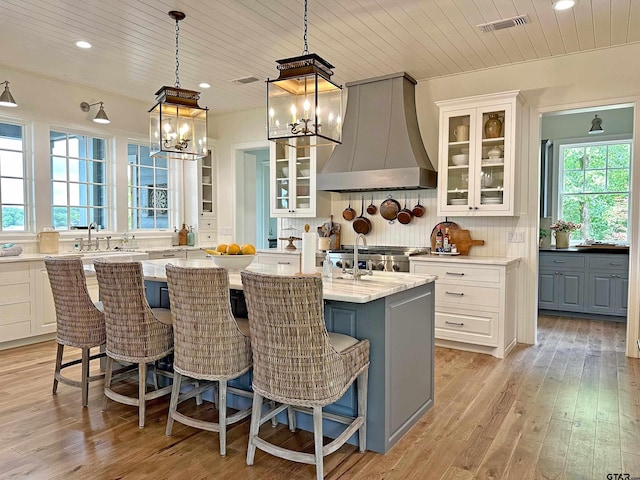 kitchen with a kitchen island, white cabinetry, custom range hood, light wood finished floors, and tasteful backsplash