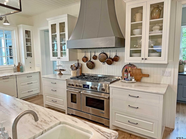 kitchen featuring white cabinetry, wall chimney range hood, double oven range, dishwasher, and light wood finished floors