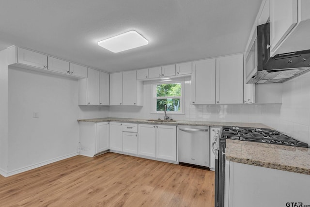 kitchen with appliances with stainless steel finishes, white cabinetry, a sink, light stone counters, and light wood-style flooring