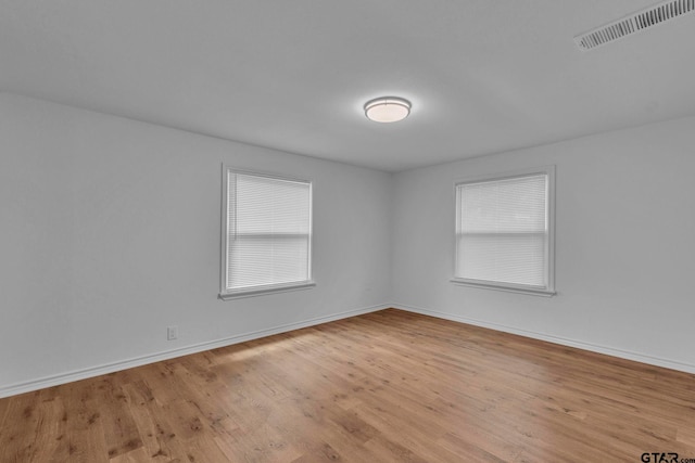 unfurnished room with baseboards, wood finished floors, and visible vents