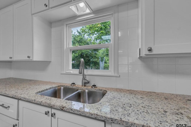 kitchen featuring a sink, backsplash, white cabinets, and light stone countertops