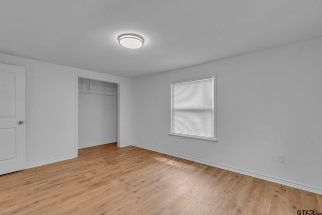 unfurnished bedroom featuring light wood-style floors, baseboards, and a closet