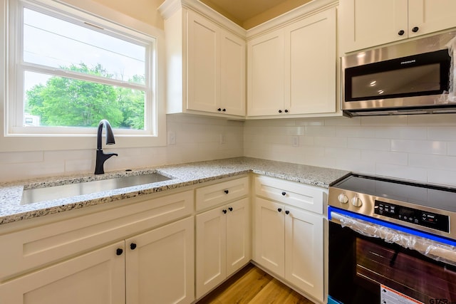 kitchen featuring white cabinets, stainless steel appliances, light hardwood / wood-style floors, and light stone counters