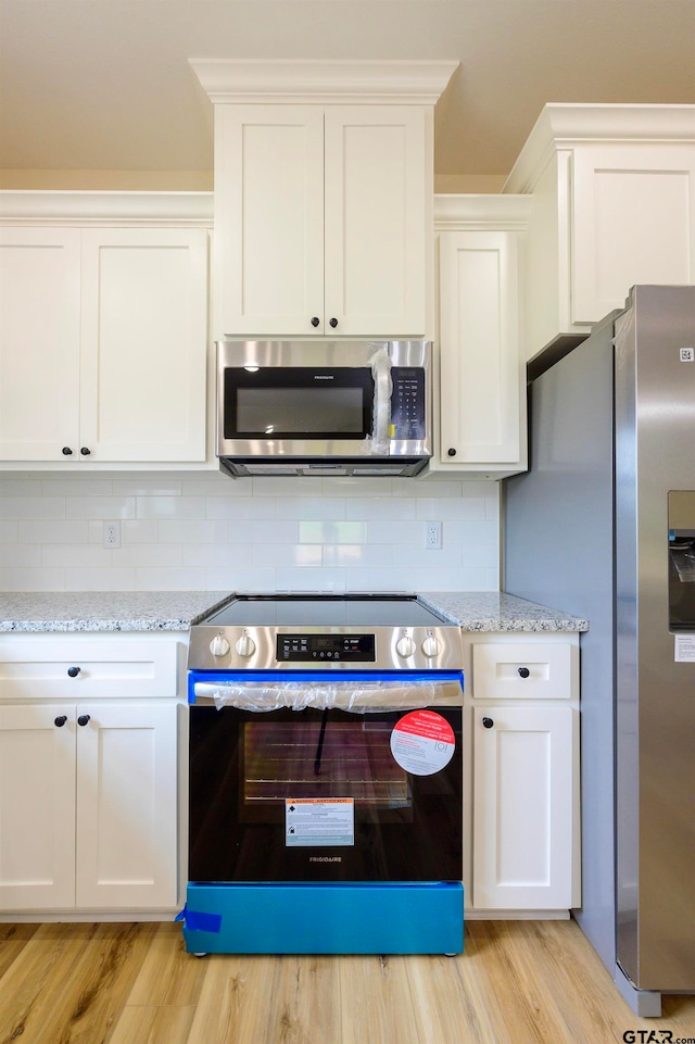 kitchen with stainless steel appliances, light hardwood / wood-style floors, light stone counters, backsplash, and white cabinets