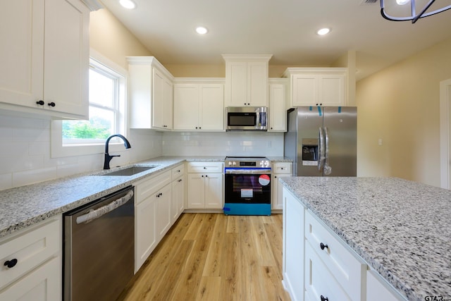 kitchen with stainless steel appliances, white cabinetry, sink, light stone countertops, and light wood-type flooring