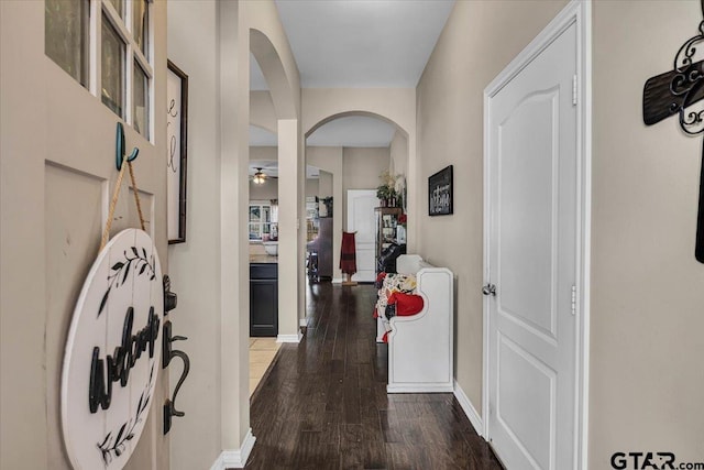 hallway with arched walkways, baseboards, and dark wood-style flooring