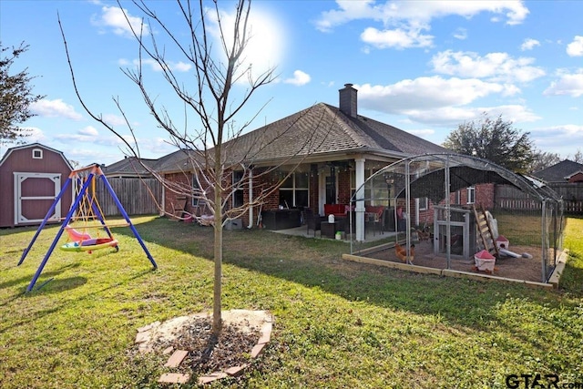 back of house featuring an outbuilding, a lawn, a fenced backyard, a playground, and brick siding