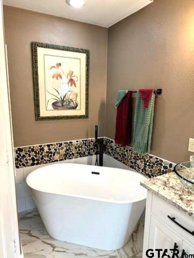 21105 Altuda Ln, Flint, TX 75762 - full bath with marble finish floors, tile walls, a freestanding tub, vanity, and wainscoting
