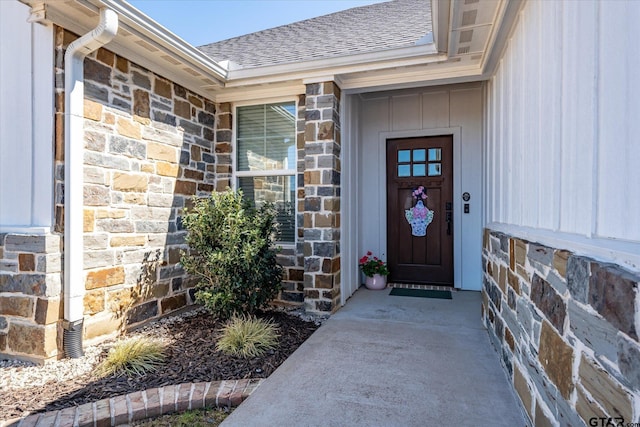 doorway to property featuring stone siding and roof with shingles