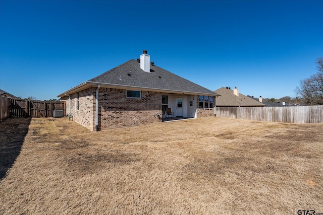 back of property featuring brick siding, a yard, a chimney, a patio, and a fenced backyard