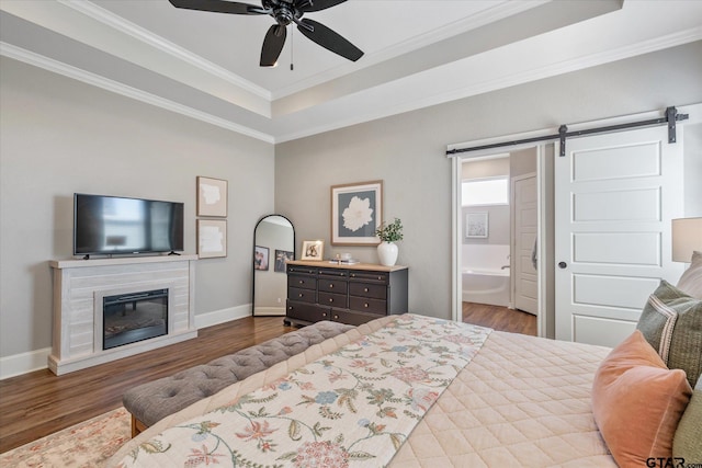 bedroom with a barn door, a glass covered fireplace, wood finished floors, baseboards, and a raised ceiling