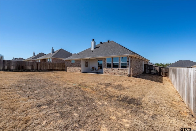 rear view of house featuring brick siding, a yard, a chimney, a patio area, and a fenced backyard