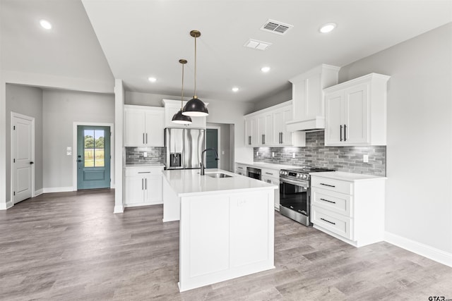 kitchen featuring white cabinets, hanging light fixtures, appliances with stainless steel finishes, and an island with sink