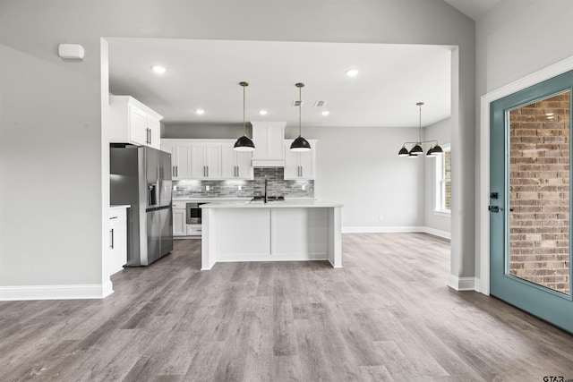 kitchen featuring stainless steel appliances, pendant lighting, light hardwood / wood-style flooring, white cabinets, and an island with sink