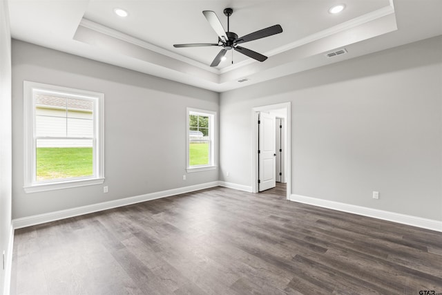 empty room with a tray ceiling, dark wood-type flooring, and ornamental molding