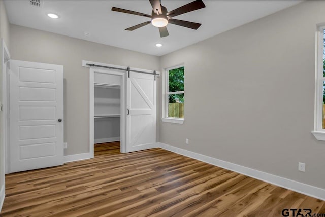 1002 E Main St, Whitehouse, TX 75791 - unfurnished bedroom featuring a barn door, baseboards, wood finished floors, and recessed lighting