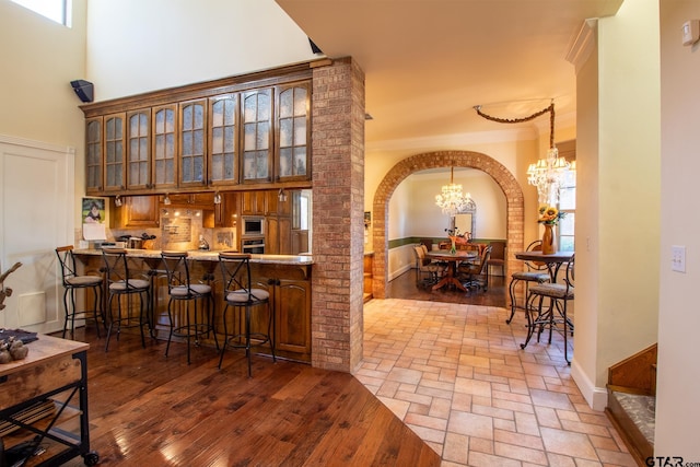 bar featuring hardwood / wood-style flooring, appliances with stainless steel finishes, ornamental molding, a towering ceiling, and a chandelier