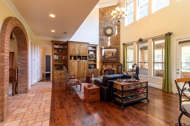 living room featuring light hardwood / wood-style floors, an inviting chandelier, crown molding, a fireplace, and a high ceiling