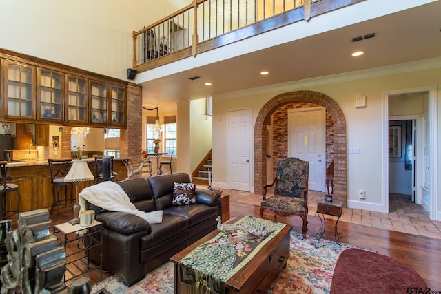 living room featuring a towering ceiling, hardwood / wood-style flooring, crown molding, and an inviting chandelier